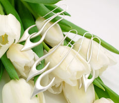 A close-up image of a bouquet of white tulips with silver earrings resting on them.