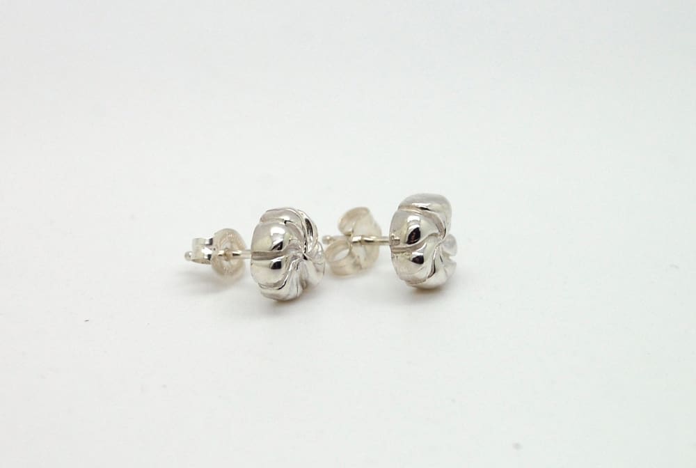 A pair of silver earrings with spiral designs on the back rests on a white surface.