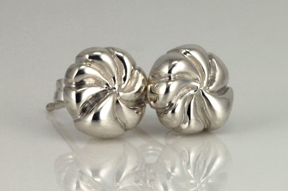 Two silver earrings with a twisted, spiral design are placed on a reflective surface.