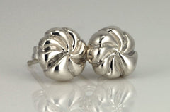 Two silver earrings with a twisted, spiral design are placed on a reflective surface.