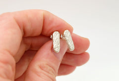 A hand holding a pair of silver earrings with a textured design.