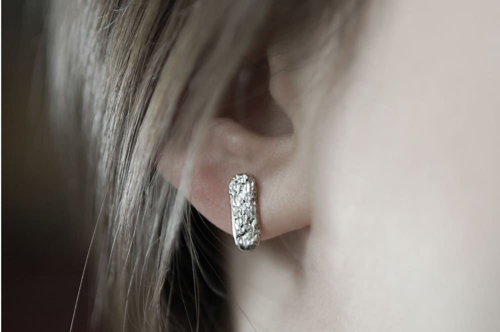 A close-up view of a person's ear adorned with a silver earring featuring a textured design.