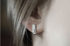 A close-up view of a person's ear adorned with a silver earring featuring a textured design.