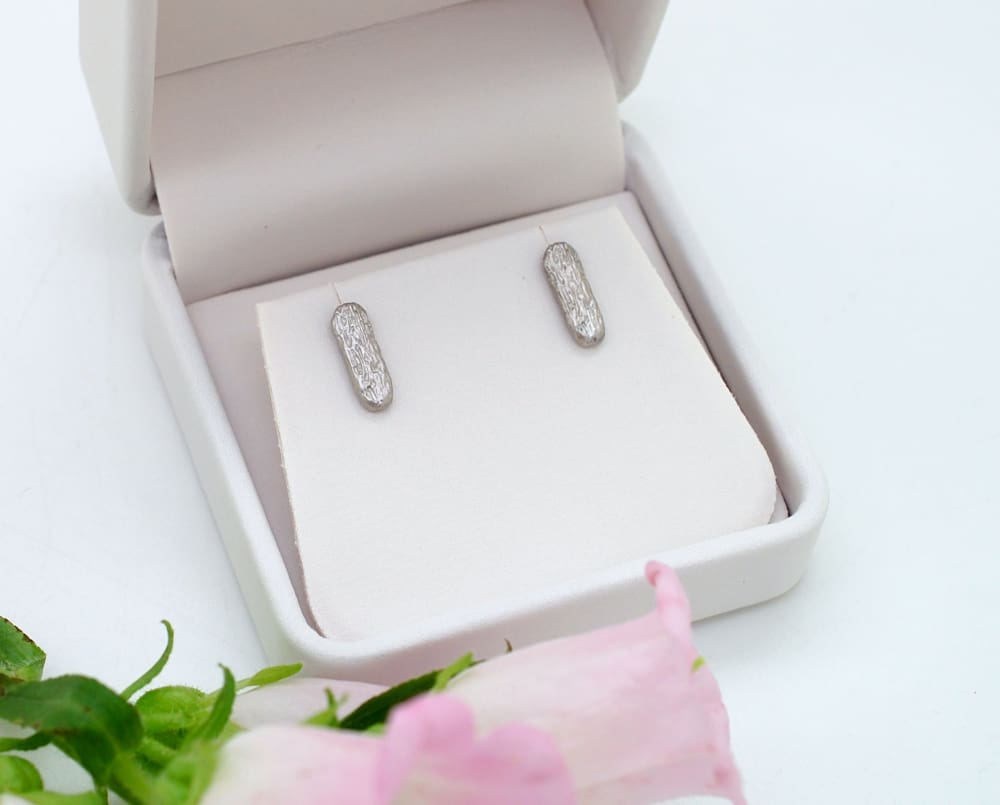 A pair of diamond earrings is displayed in a white jewelry box, with a pink flower in the foreground.