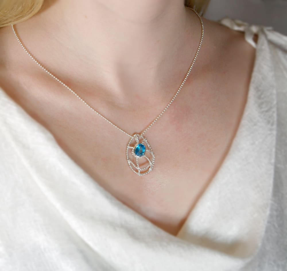 A close-up view of a woman's neck and chest wearing a silver necklace with a blue gemstone pendant.