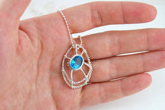 A hand holding a silver necklace with a blue gemstone pendant.