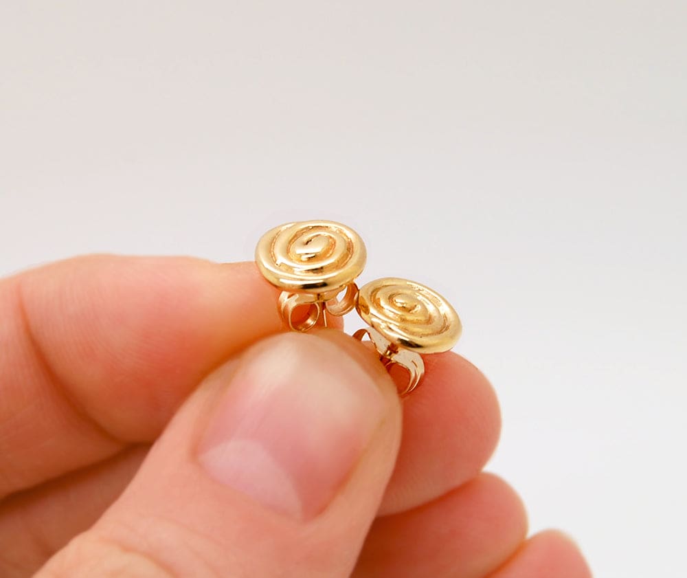 A hand holding a pair of gold earrings with spiral designs.